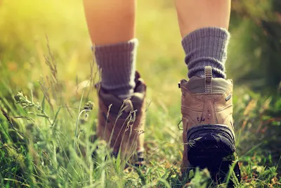 Young woman hiker in hiking socks and boots walking on trail in grassland
